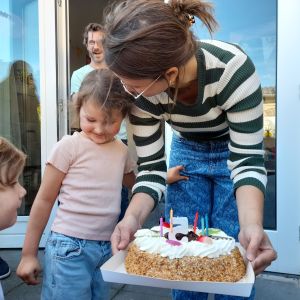 Nora blies de 5 kaarsjes uit op de taart die Lois vasthoudt. Boven hen Rommert.