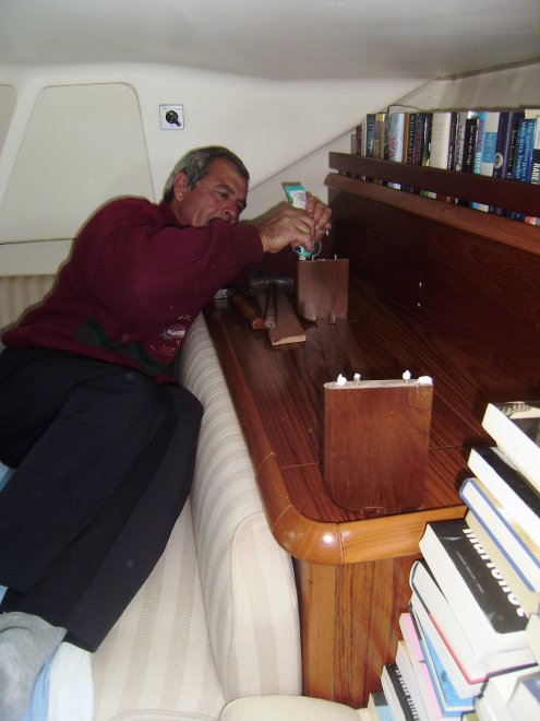 Peter Samba de timmerman smeert lijm bij de stalen staafjes, die de nieuwe boekenhouder op zijn plaats moeten houden. Niet een erg doordachte constructie