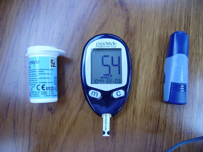Vandaag was mijn nuchter bloedsuiker 5,4 mmol/l. Links het doosje met teststrips, midden het meetapparaatje met een teststrip erin geschoven, rechts het prikapparaatje