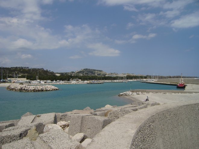 Invaart van Rocella Ionica. Als je scherp kijkt zie je aan de lichtere kleuring van het water op de voorgrond hoe ondiep het daar is. Blijf dus dichtbij het linker (rode) havenhoofd als je binnenvaart