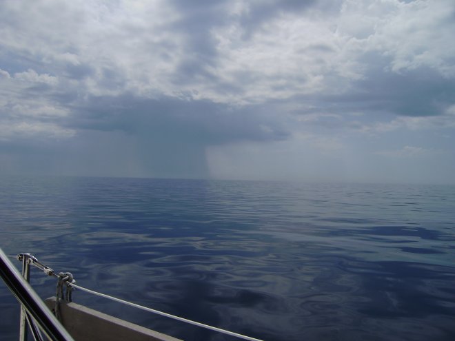 Aan stuurboord hangt het grijze gordijn van een regenbui onder een donkere wolk