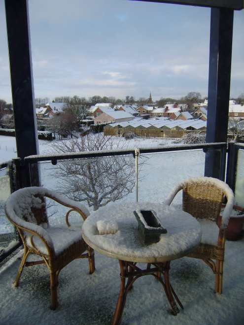 Sneeuw op ons balkon aan de dijkkant. Gezicht op Andel. In de verte de spits van de Romboutstoren