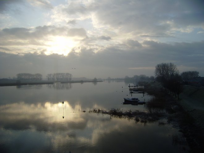 Er hangt een lichte nevel boven de rivier. Het water is hoog. Het baken op de krib staat in het water
