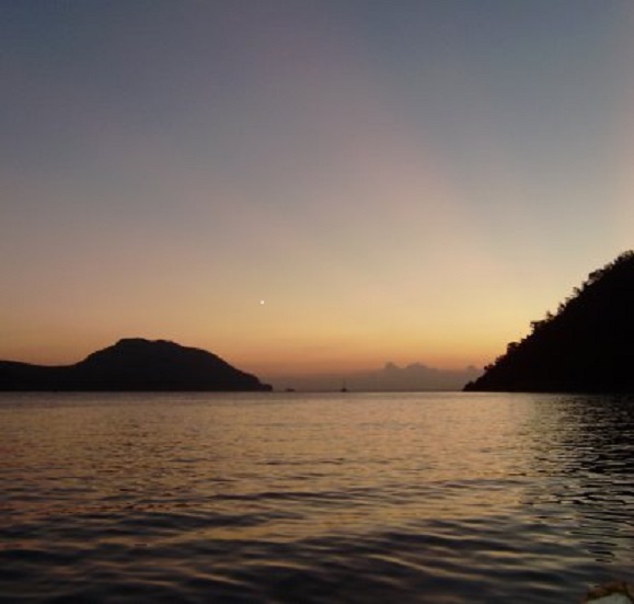 Bij het ochtendkrieken vertrekt Anégada. Wie goed kijkt ziet iets links in de uitvaart van de baai een stipje. Dat zijn ze. Het lijkt rustig, maar buitengaats is harde wind en een nare zeegang