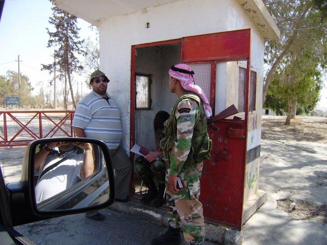 Paspoortcontrôle bij een road block voor de dam van het Al-Assad stuwmeer. De zittende soldaat schrijft onze gegevens over in een dik schrift. Links Nourairi, onze chaufeur. In de zijspiegel van de auto zie je mij nog net