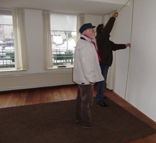 In ons toekomstig appartementje neemt de timmerman de maat voor de boekenkasten. Dat bruine kleed, dat gaat zeker weg. De houten vloer mag blijven. De ramen aan deze kant geven uitzicht op het sluisje naar de Merwede