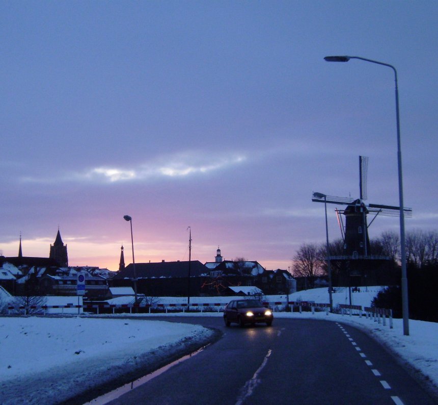 Spijksedijk. tegen de gloed van de ondergaande zon tekenen zich boven de stad dezelfde vier torens af als op de foto van gisteren. Vlnr. de Kapeltoren, de Grote Toren en twee waarvan ik de namen nog niet weet. Helemaal rechts de stadsmolen Nooit Volmaakt