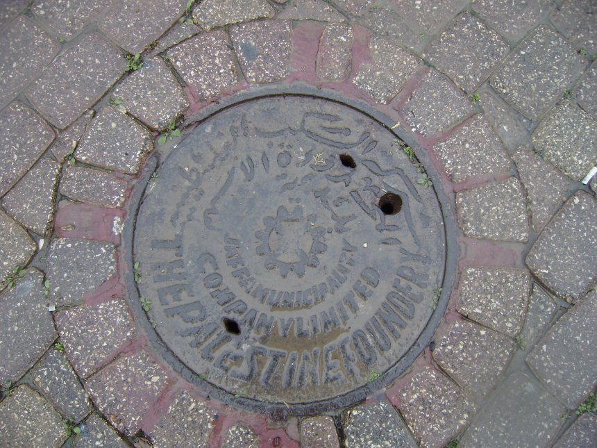 Putdeksel uit de Britse Mandaatperiode in het oude centrum van Ashkelon. Tekst in het Arabisch (boven) en het Engels. Geen Hebreeuws dus