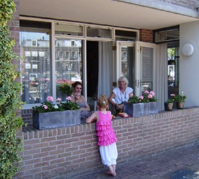 Barbara en Ans in de schaduw op onze veranda. Ervoor staat de kleine Esri. de huizen aan de Kriekenmarkt weerspiegelen zich in de ramen