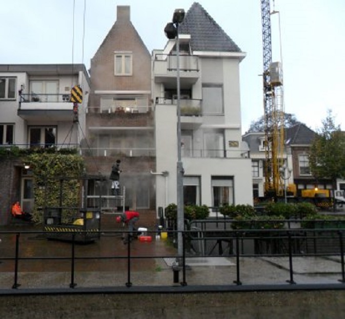 Met een hogedrukspuit wordt onze gevel gereinigd. Rechts de hoge kraan