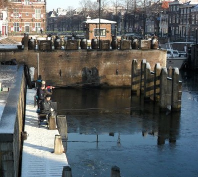 Ondanks een dun ijslaagje in de haven, zit men toch gewoon te vissen.