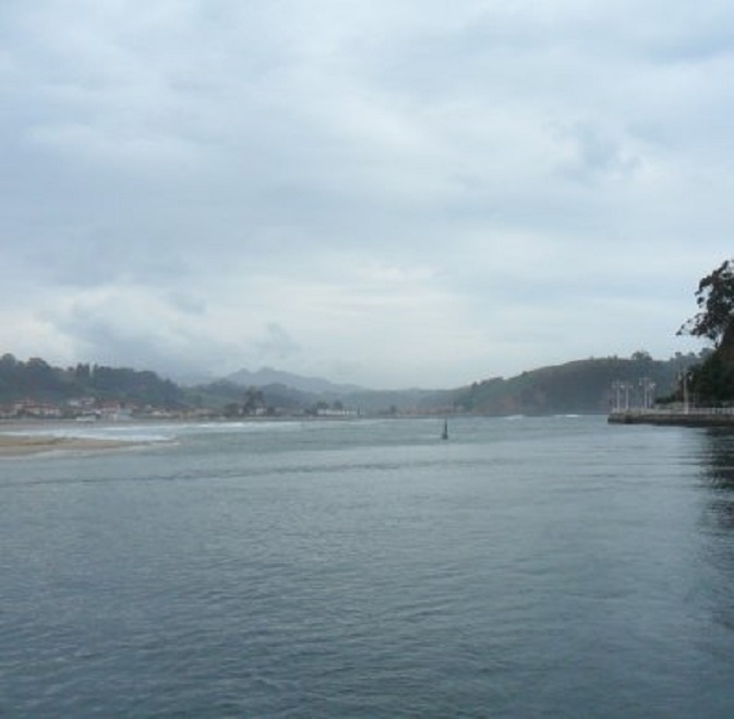 Invaart Ribadesella (terugblik). Midden een groen boei, Daarachter de hoge zeegang en links het strand en de zandbanken, waar de brekers op uitvloeien.