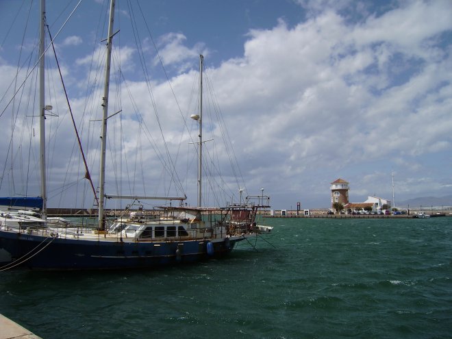 Eén van de roestbakken in de haven van Almérimar. Ooit een mooie tweemaster geweest. Op de achtergrond het havenkantoor. Het waait Bf 8 - 9