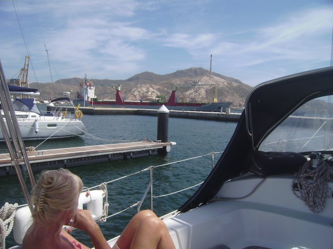 Uitzicht vanuit de Yacht Port Marina van Cartagena. Twee sleepboten trekken op de achtergrond een bulkcarrier naar buiten