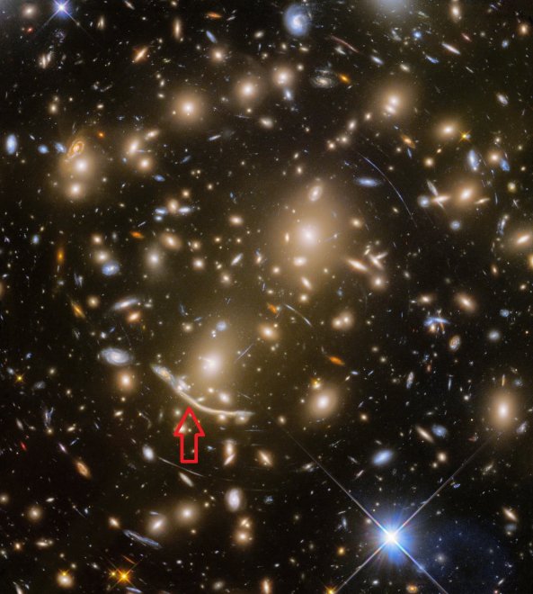 Abell 370, een cluster van sterrenstelsels, met bij de rode pijl een superoud spiraalstelsel in zijaanzicht, dat zichtbaar is door de zwaartekrachtlens van Abell (foto: Hubble)