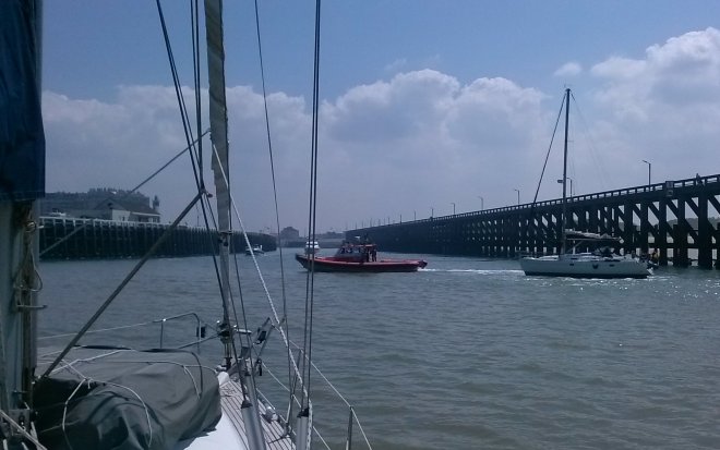 Invaart van Blankenberge. Het jacht voor ons zit vast op de nieuwe zandbank, die de doorvaart afsluit. Een boot van de havendienst probeert vergeefs hem vlot te trekken.