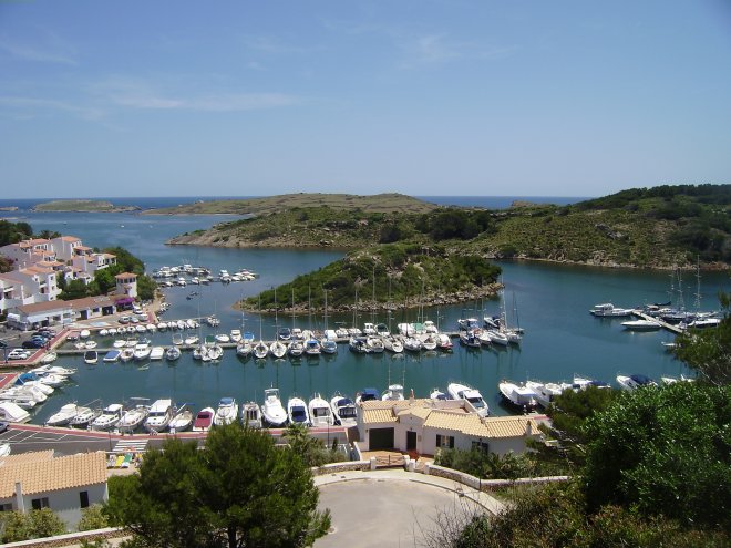 De kleine haven van Addaya. Links het havenkantoor bij het torentje, In het midden het eilandje van Ses Monas. Helemaal rechts ligt onze Dulce naast de kop van het steigertje. In de verte de zee