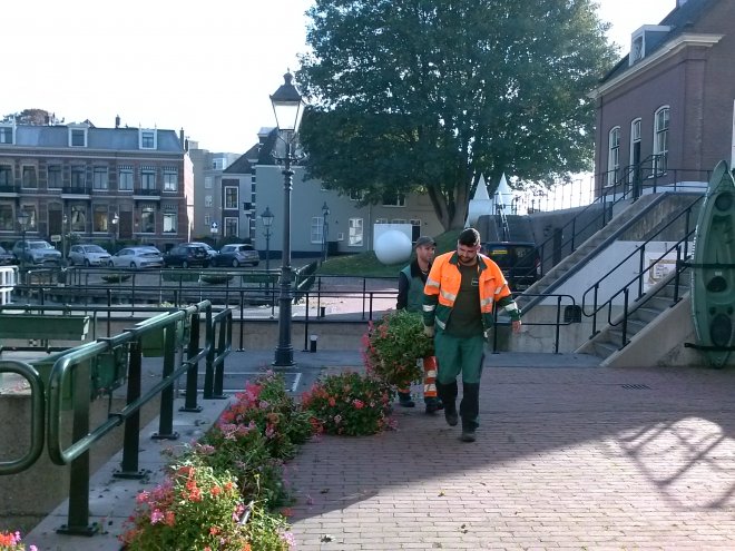 Mannen van de groendienst halen de bakken met geraniums op de sluis leeg.