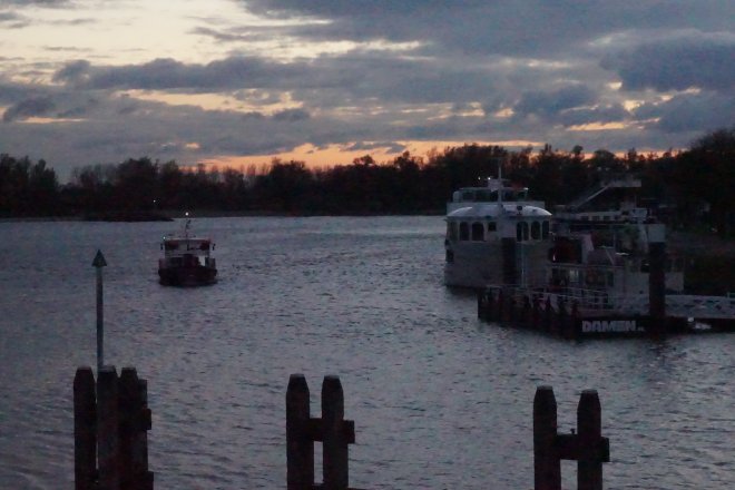 De avond valt over de Merwede. Het pontje van Sleeuwijk komt aanvaren. Rechts ligt een cruiseschip aangemeerd.