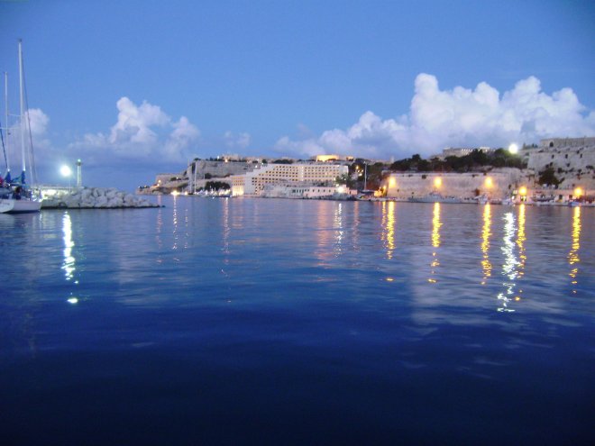 Dit is ons uitzicht. De avond valt boven Valletta (rechts) en de havenuitgang naar zee