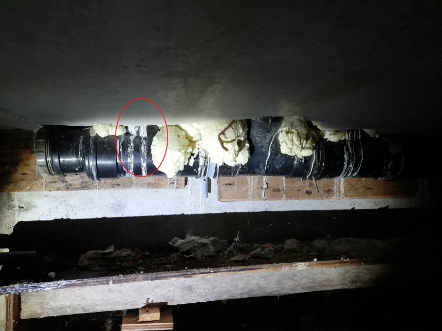 De grote rioolafvoerbuis in de kruipruimte onder ons pand. Rode cirkel: de verstopte afvoer van boven. De witte proppen om de buis heen is pur.