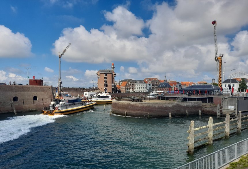 Overzicht van zeefront Vlissingen. Er vaart juist een loods naar binnen. rechts ervan Brasserie Evertsen en rechts daarvan het keersluisje met de invaart van onze haven en erboven de Hell Raider van de kermis.